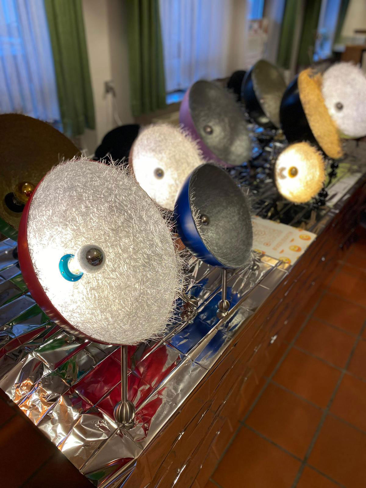 Mehrere bunte Lampen mit flauschigen Schirmen stehen auf einem metallischen Tisch