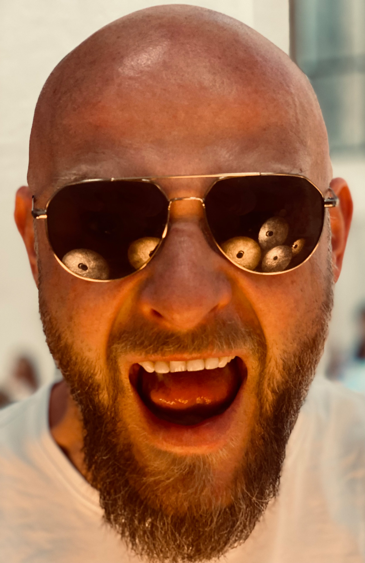 Kahlkoepfiger Mann mit Bart schreit, goldene Sonnenbrille mit Augenreflexen